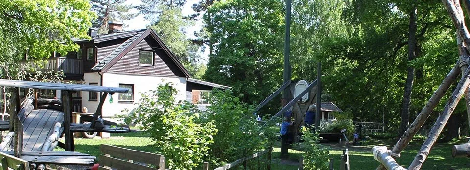 Förskolans huvudbyggnad och gård med träd