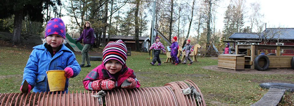 Två barn i vinterkläder leker på förskolegården